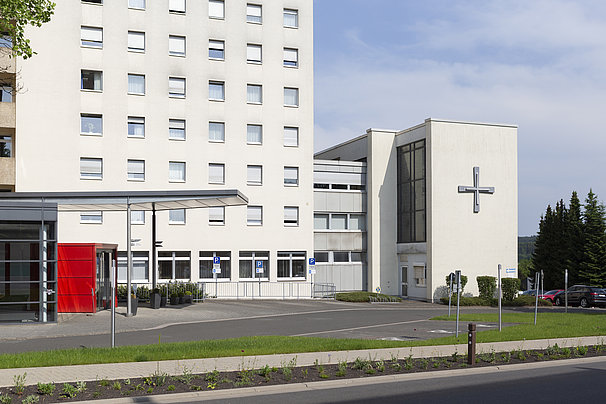 Krankenhausgebäude mit mehreren Stockwerken, Parkplätzen und einem großen Kreuz an der Fassade