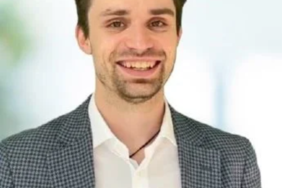 Porträt von Timo Sonntag, lächelnder Mann mit dunklem Haar, weißem Hemd und kariertem Sakko