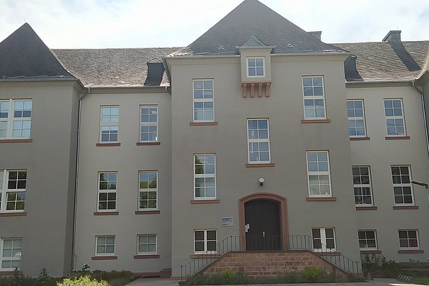 Mehrstöckiges Gebäude mit grauer Fassade und mehreren Fenstern in Trier, mit einem zentralen Eingang und Treppen davor