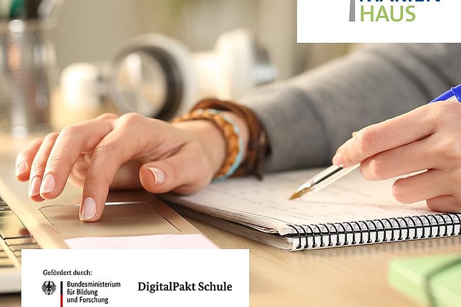 Person schreibt mit blauem Stift in Spiralnotizbuch, daneben Logo Marienhaus und Hinweis auf Förderung durch DigitalPakt Schule des Bundesministeriums für Bildung und Forschung