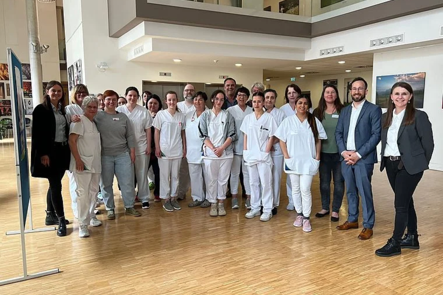 Gruppenfoto von mehreren Personen, darunter medizinisches Personal in weißer Arbeitskleidung und weitere Personen in Business-Kleidung, in einem modernen Innenraum mit Holzfußboden