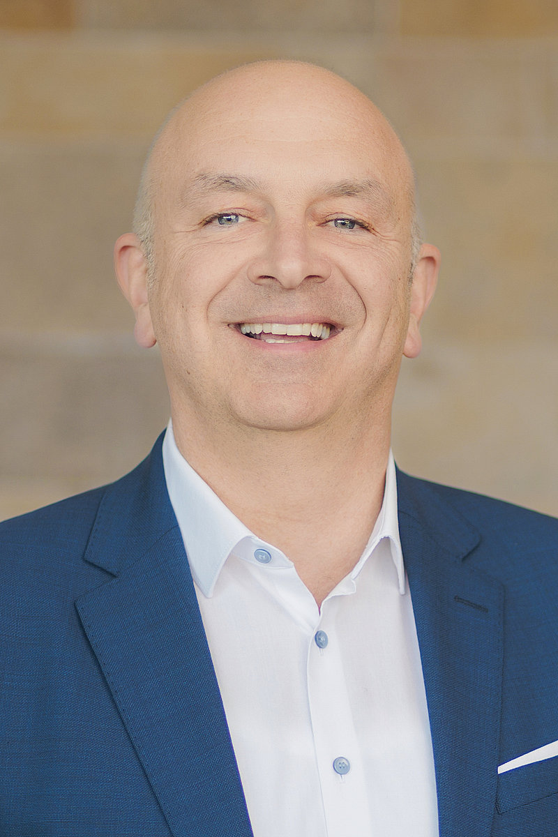 Lächelnder Alexander Schuler mit Glatze, weißem Hemd und dunklem Sakko