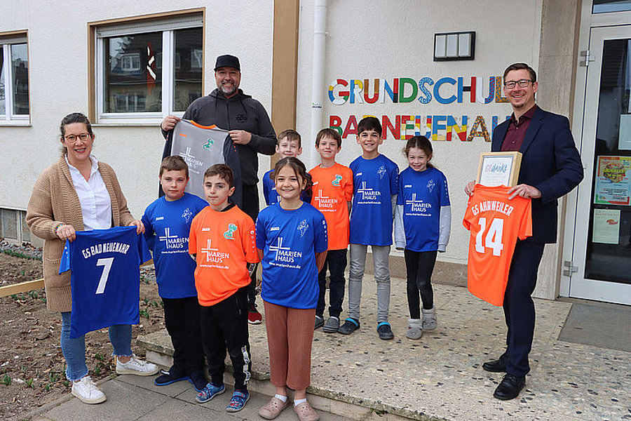 Gruppe von Kindern und Erwachsenen vor der Grundschule Bannflehen mit buntem Schriftzug, einige halten bunte Sporttrikots mit Nummern