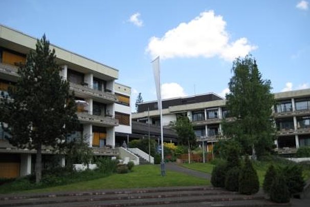 Mehrere mehrstöckige Gebäude mit Balkonen und gelben Markisen umgeben von Bäumen und Grünflächen unter blauem Himmel mit Wolken.
