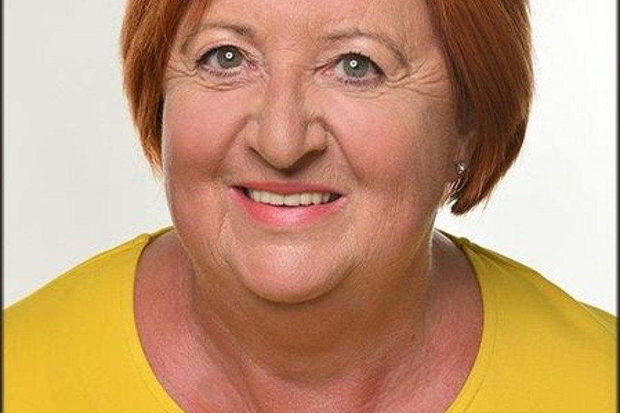 Porträt einer lächelnden Frau (Sonja Petit) mit kurzen roten Haaren und gelber Bluse vor hellem Hintergrund