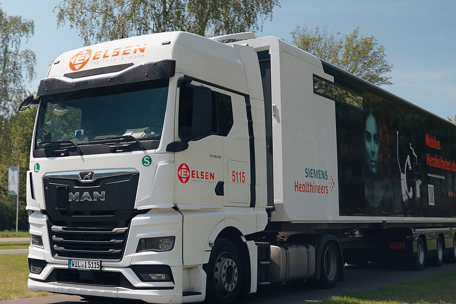 Weißer MAN-Lkw mit Aufschrift 'Elsen' und 'Siemens Healthineers' steht auf einer Straße, Anhänger zeigt medizinische Grafiken