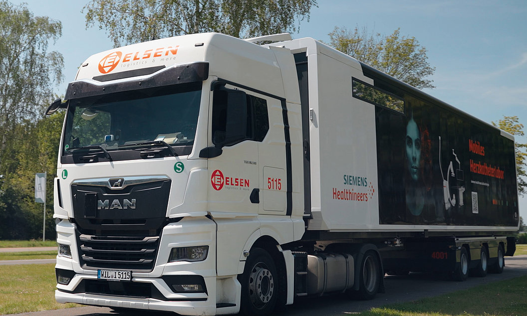 Weißer MAN-Lkw mit Aufschrift 'Elsen' und 'Siemens Healthineers' steht auf einer Straße, Anhänger zeigt medizinische Grafiken