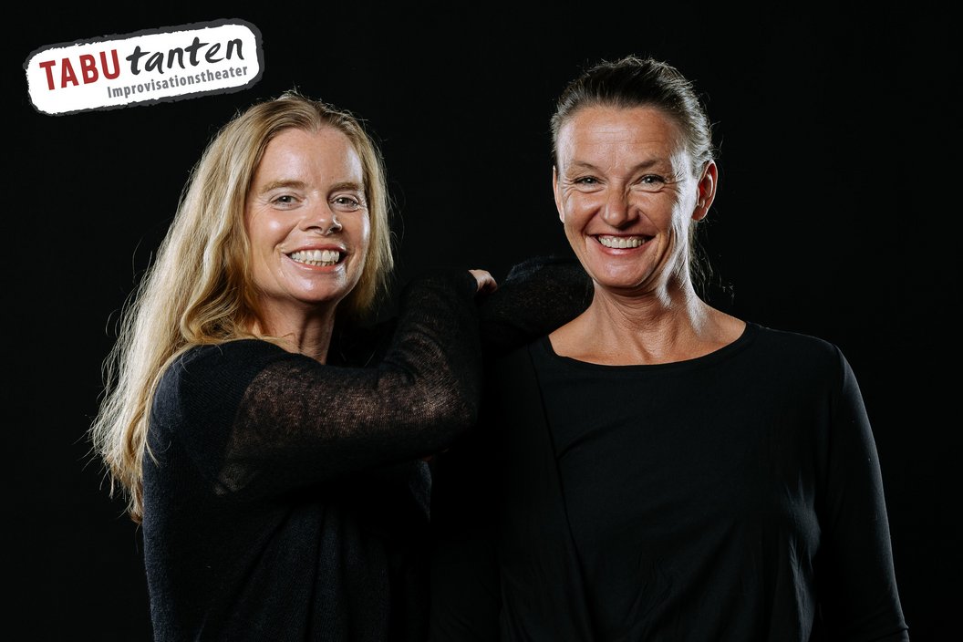 Zwei Frauen in schwarzer Kleidung vor schwarzem Hintergrund, eine mit langen blonden Haaren, die andere mit zurückgebundenem Haar. Logo 'TABUtanten Improvisationstheater' oben links.