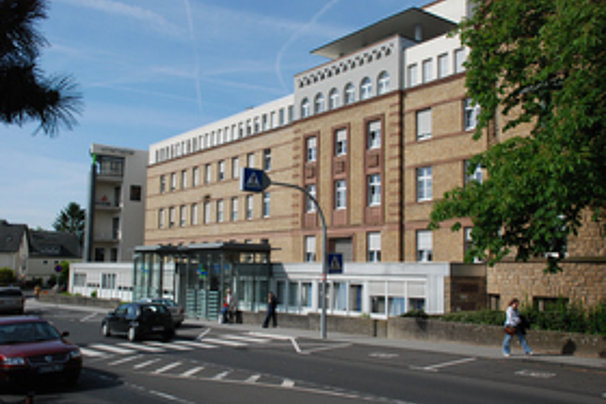 Mehrstöckiges Gebäude mit brauner Fassade und weißen Fenstern an einer Straße mit Fußgänger und parkenden Autos