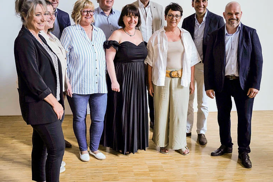 Neun Personen in formeller Kleidung bei der Eröffnung der Herzinsuffizienzeinheit, stehend auf Holzboden vor weißer Wand
