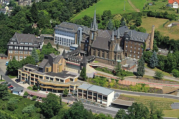 Luftaufnahme eines historischen Gebäudekomplexes mit Kirche, modernen Gebäuden und grüner Umgebung