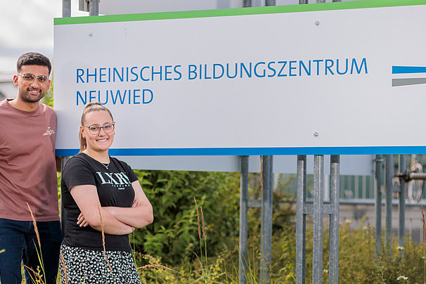 Zwei Personen stehen neben einem Schild mit der Aufschrift 'Rheinisches Bildungszentrum Neuwied' und dem Logo von Marien Haus vor einem Gebäude.