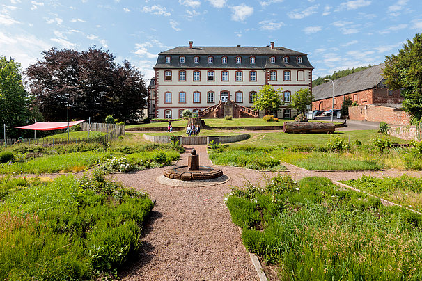 Historisches Herrenhaus mit symmetrischem Garten und Brunnen im Vordergrund bei sonnigem Himmel