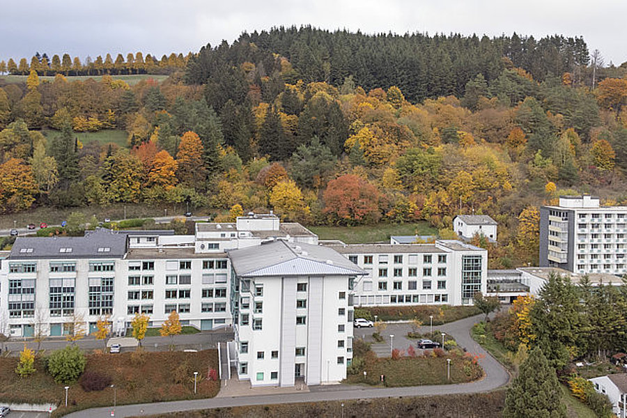 Mehrere weiße Gebäude vor einem bewaldeten Hügel mit herbstlich gefärbtem Laub