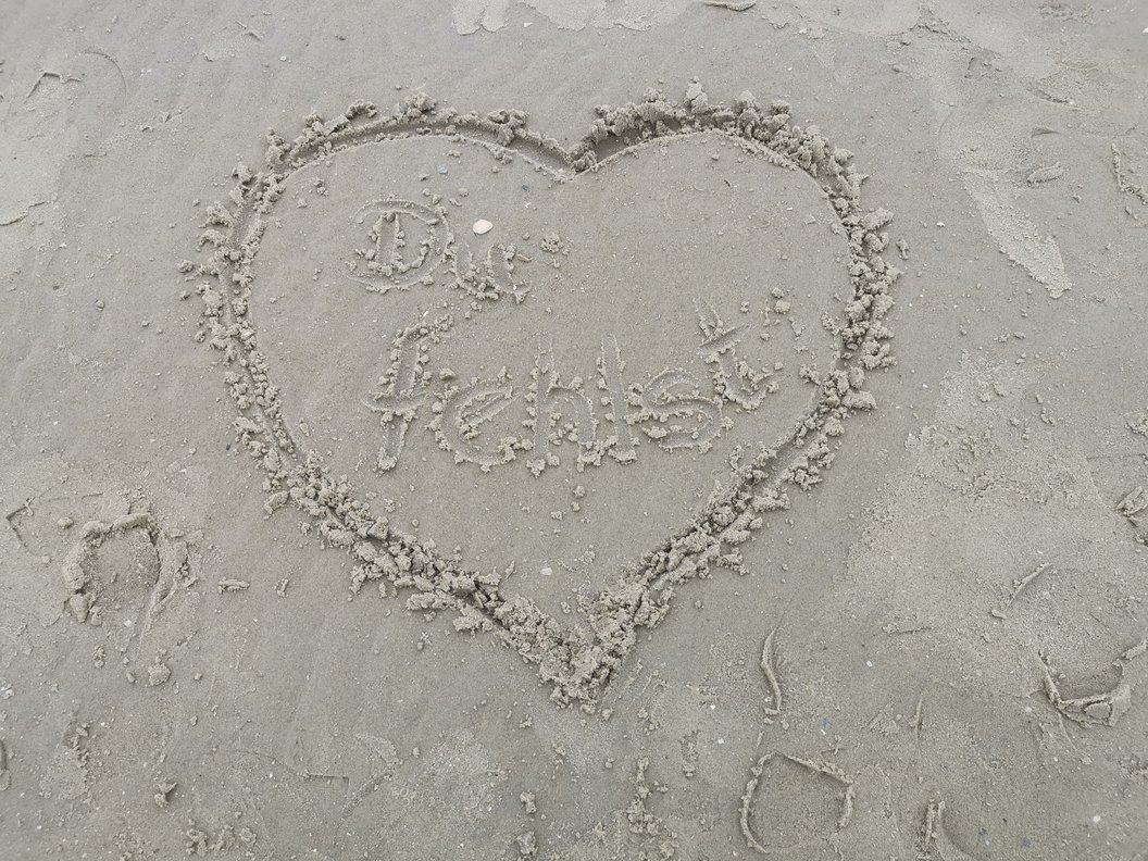 Herz in den Sand gezeichnet mit der Aufschrift 'Du fehlst'