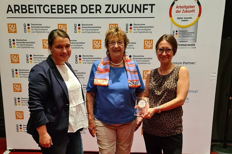 Drei Frauen stehen vor einer Wand mit dem Schriftzug 'Arbeitgeber der Zukunft' und Logos des Deutschen Instituts für Nachhaltigkeit und Digitalisierung, eine Frau hält eine Auszeichnung.