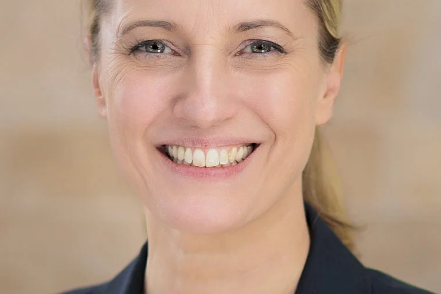 Porträt von Sandra Postel, lächelnde Frau mit blonden Haaren, trägt dunklen Blazer und weiße Bluse