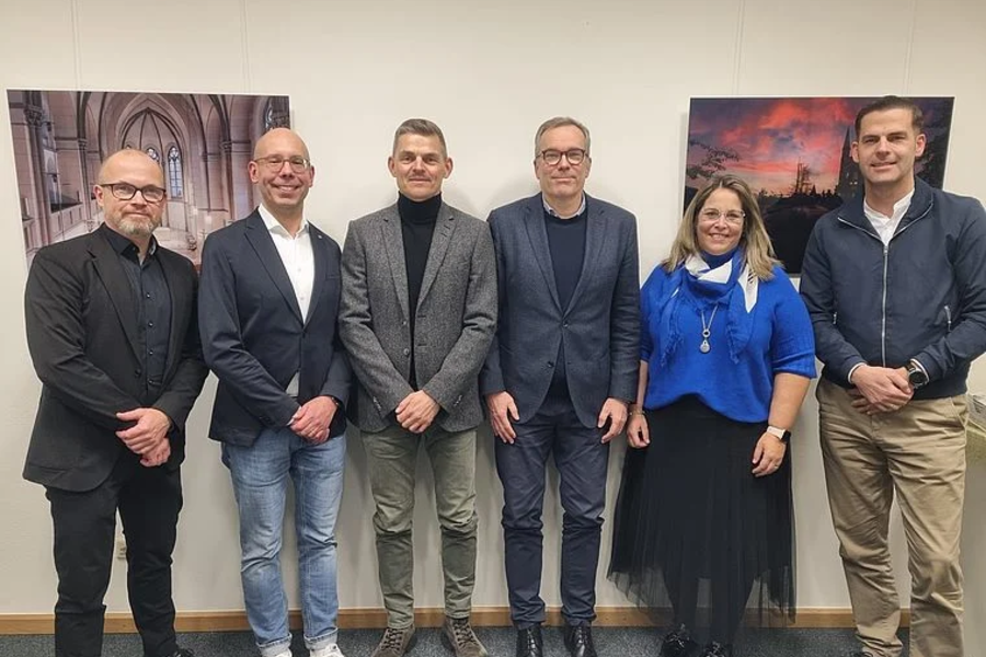 Sechs Personen des medizinischen Beirats stehen nebeneinander vor einer Wand mit zwei großen Bildern, formell gekleidet, in einem Innenraum.